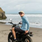 Man in cap riding motorcycle on beach. Moto cross dirtbiker on beach sunset on Bali. Young hipster